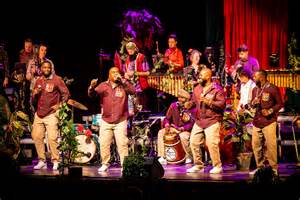 Een ensemble van blazers in concertkleding, spelend op een podium.
