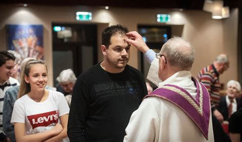 Handen die een askruisje ontvangen op het voorhoofd.
