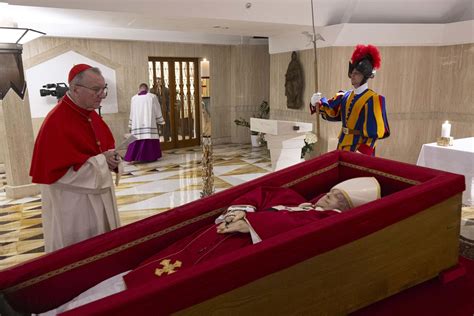 Een afbeelding van een katholieke priester die wijwater besprenkelt over een kist.
