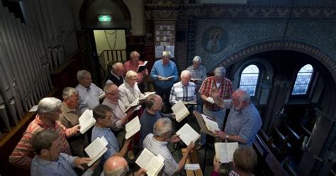 Foto van een koor dat repeteert in een kerkelijke setting.