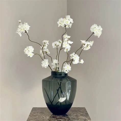 Een bloemstuk met witte bloesemtakken en een witte kaars