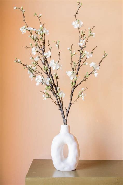 Symbolische bloemenschikking met witte bloesemtakken en een witte kaars in een kerkelijke setting.